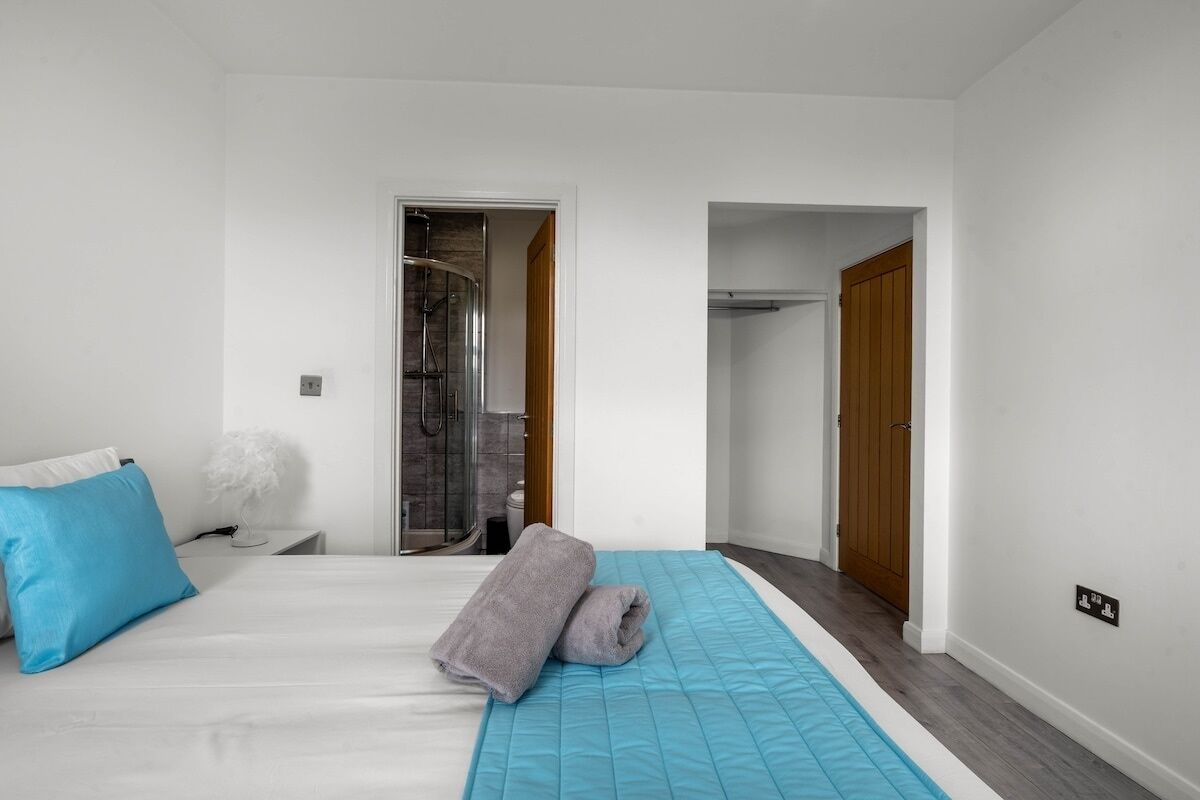 Un dormitorio con una cama, una colcha azul, una toalla gris, una lámpara blanca y un rincón de ducha.