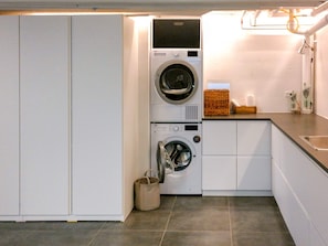 A compact laundry area with a front-loading washer and dryer, a small sink, and a tiled floor.