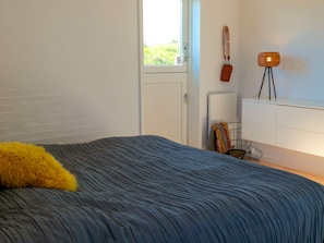 A bedroom with a bed, a window, a radiator, a lamp, and a door.