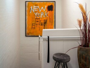 A room with a white wall, a framed artwork with text, a white cabinet, and a stool with a potted plant.