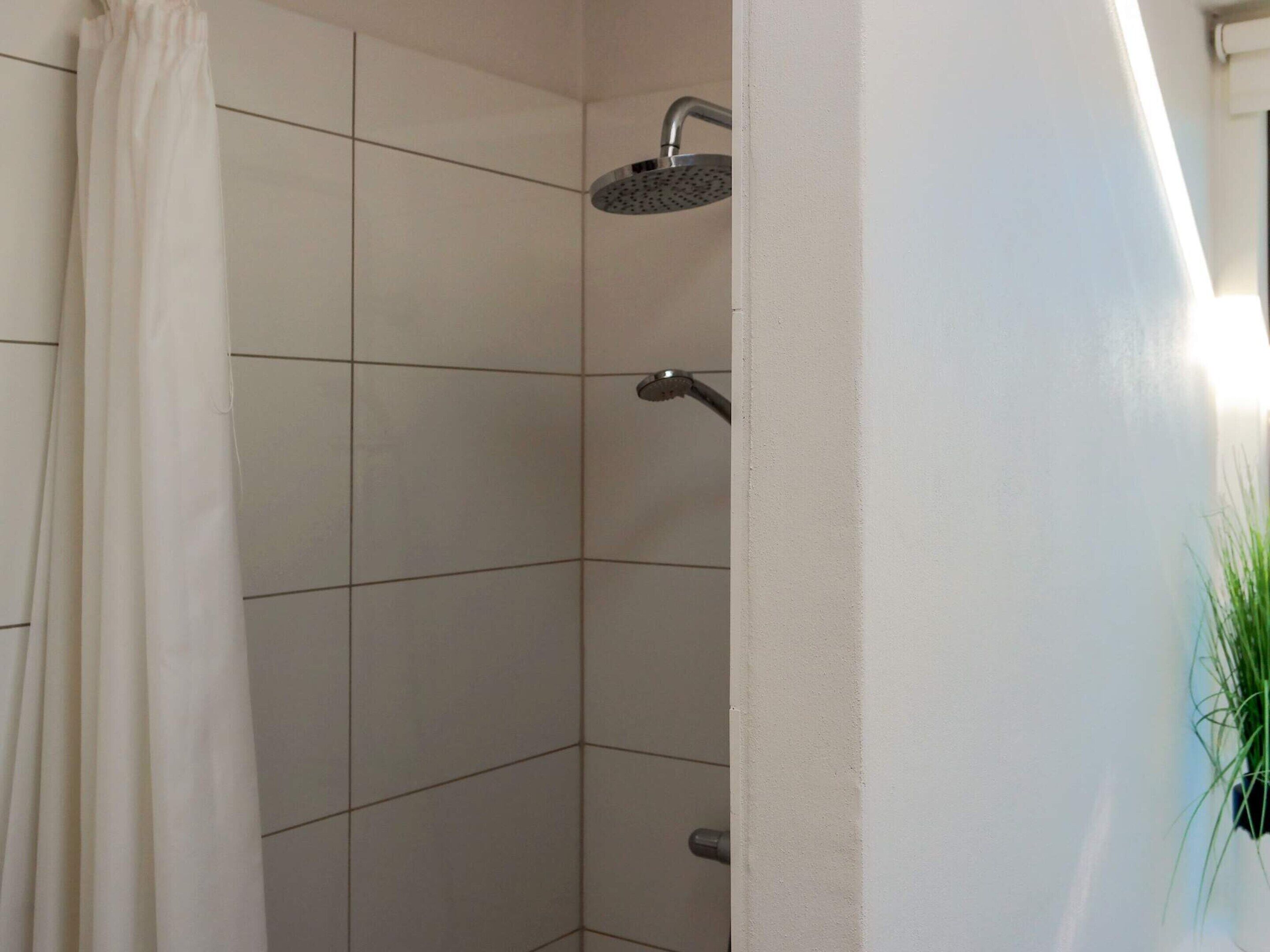 A shower area with white tiles, a showerhead, and a curtain.