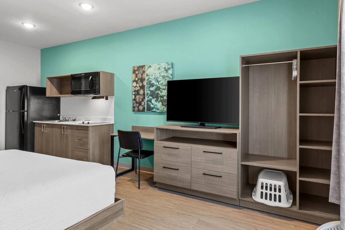 Una habitación de hotel moderna con cama, kitchenette, televisor y armario.