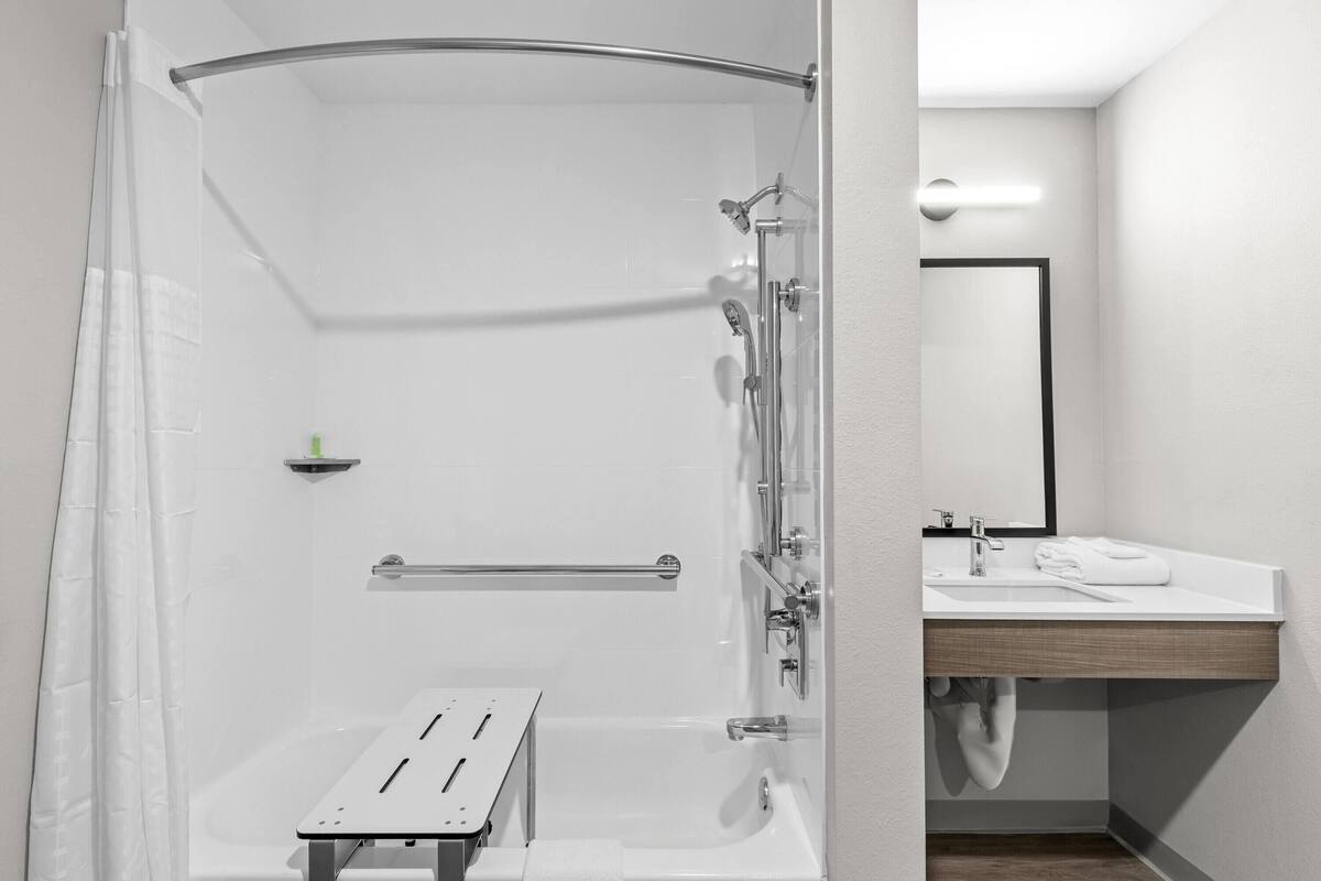 Un baño moderno con cabina de ducha de vidrio, una bañera, tocador con espejo y perchero para toallas.