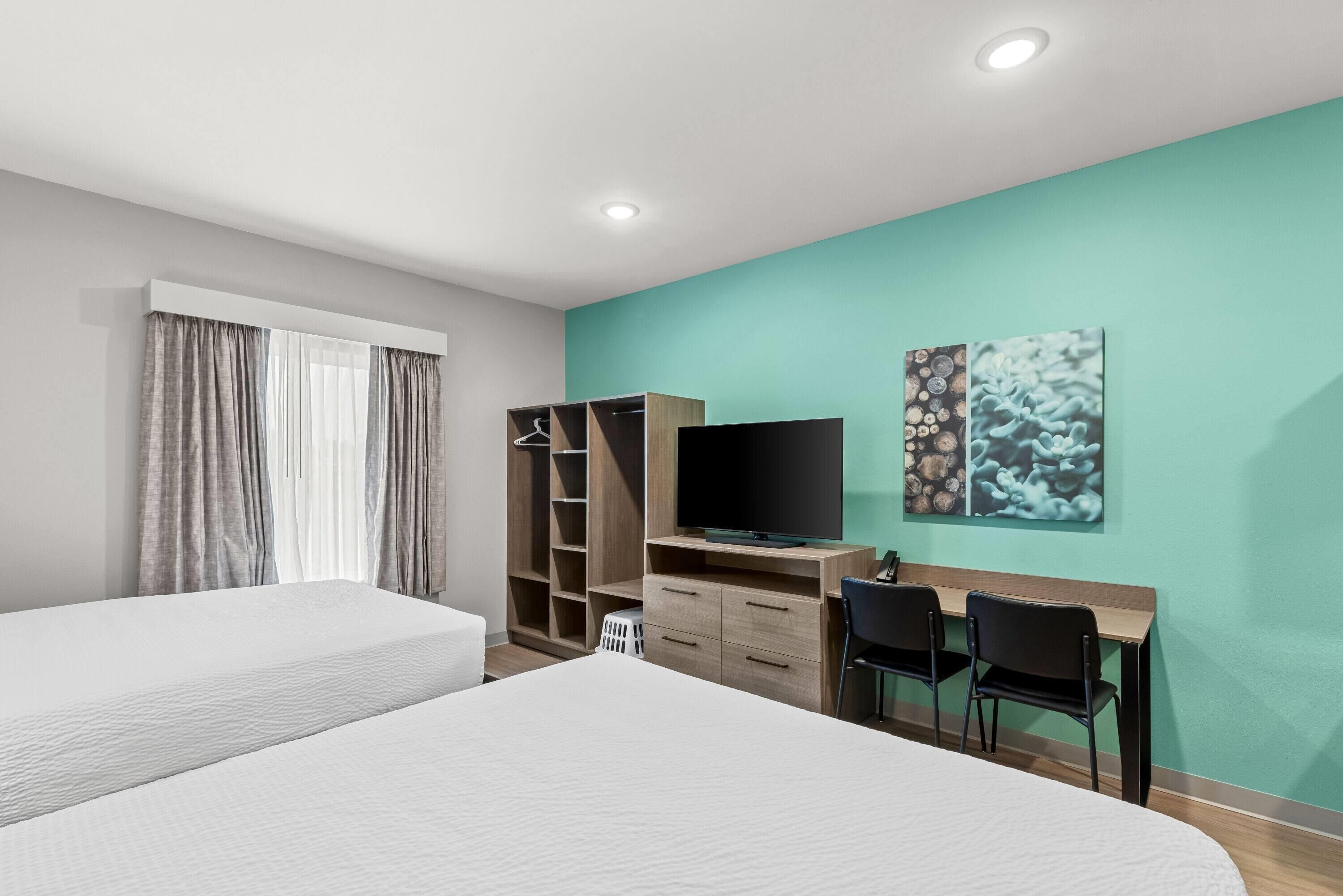Une chambre d’hôtel avec deux lits, un bureau avec des chaises, une télévision et une armoire.