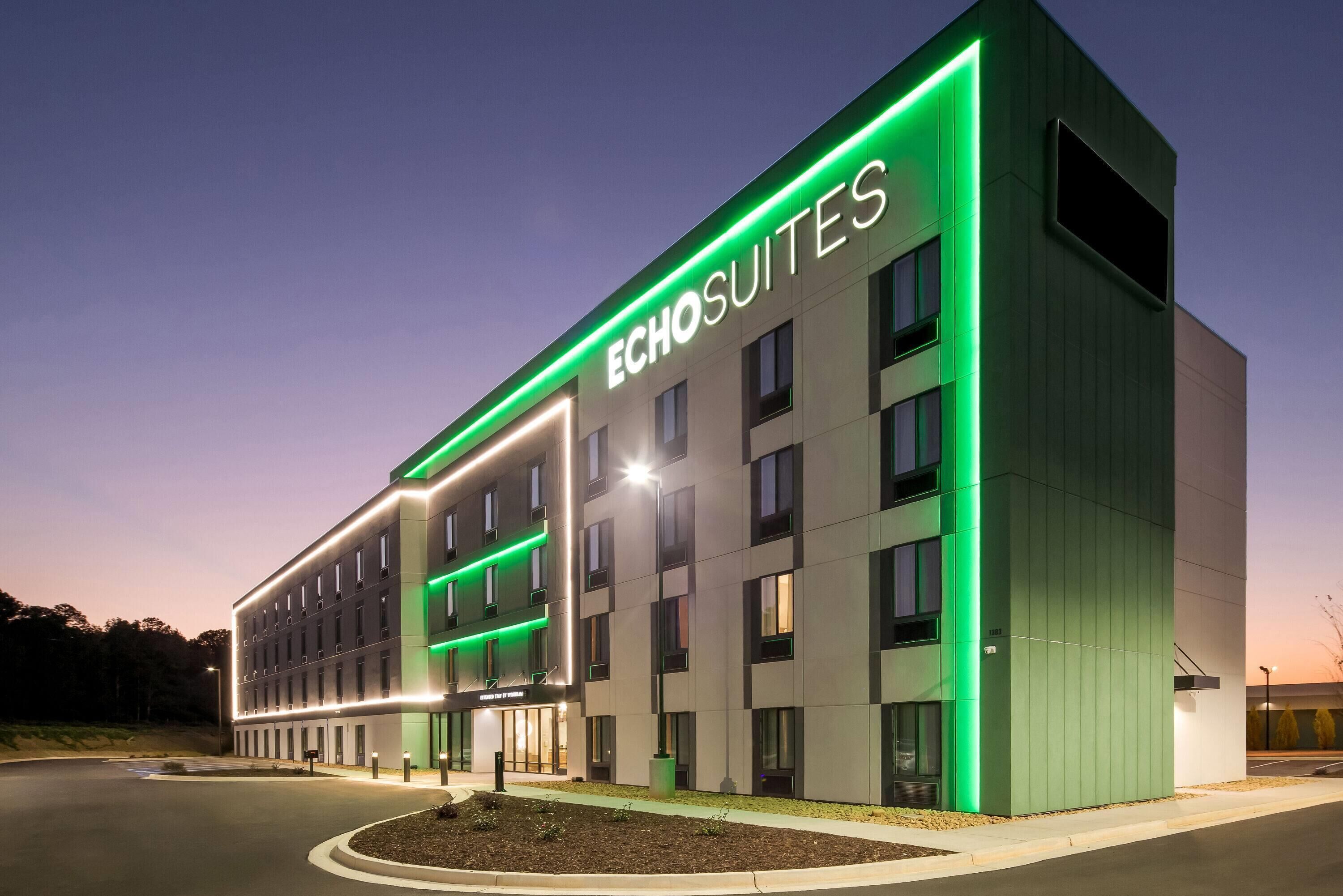 Un hotel moderno con un'imponente insegna 'Echosuites', caratterizzato da un design pulito e rettangolare, con numerose finestre e un ingresso ben illuminato.