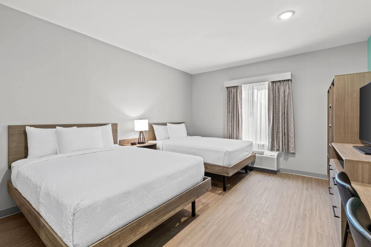 Habitación de hotel con dos camas, un escritorio, una silla, un televisor y una ventana con cortinas.
