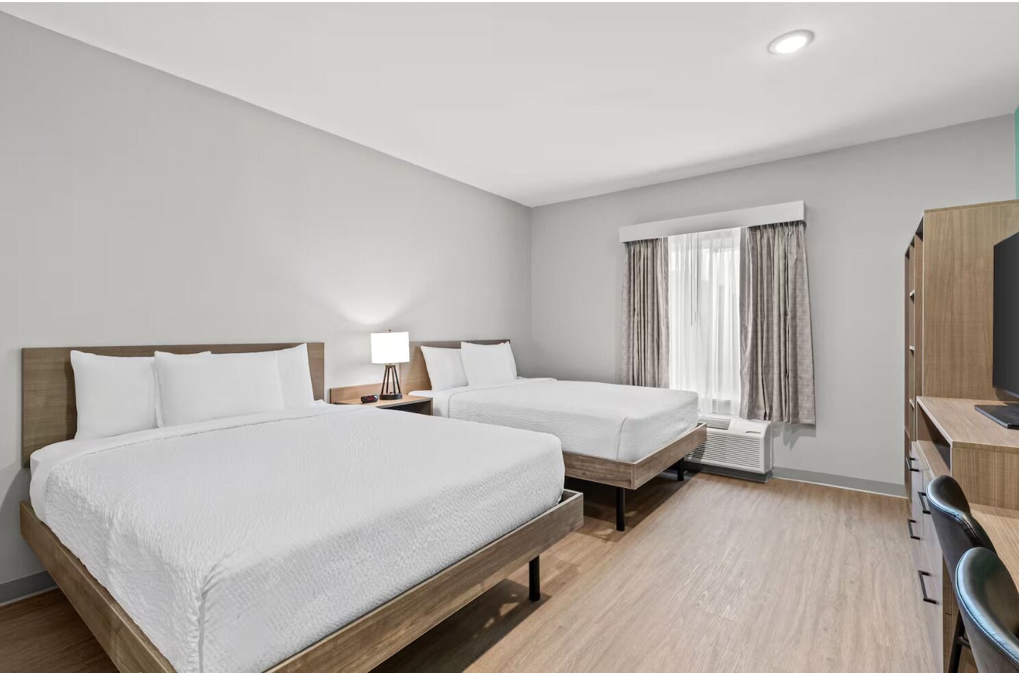 Habitación de hotel con dos camas, un escritorio, una silla, una lámpara y una ventana con cortinas.