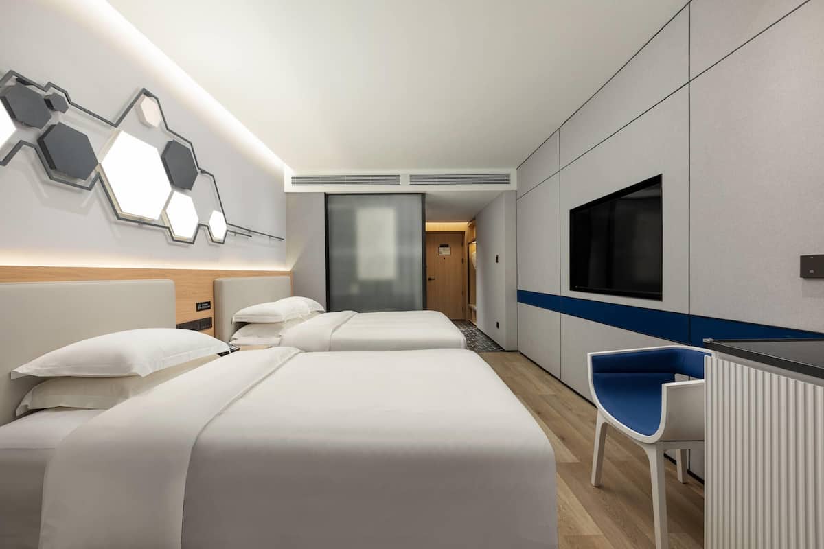 A modern hotel room with two beds, a desk, and a TV.