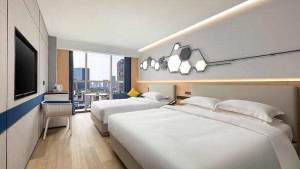 Une chambre d’hôtel moderne dotée de deux lits, d’un téléviseur à écran plat, d’un bureau avec une chaise et offrant une vue sur la ville.