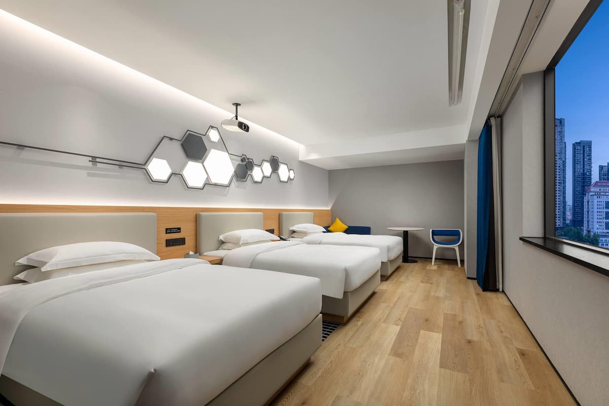 A modern hotel room with three beds, a small table, and a chair.