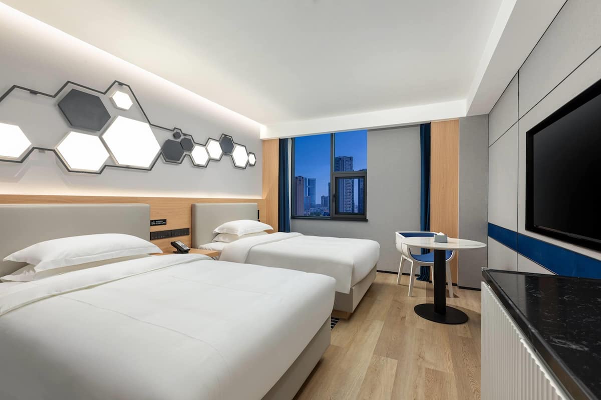 A modern hotel room with two beds, a desk, and a large TV.