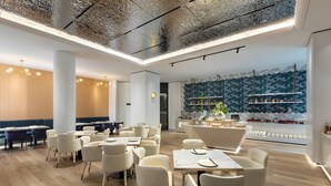 Un restaurant moderne avec des chaises et des tables blanches, un bar et une cuisine visible au fond de la salle.