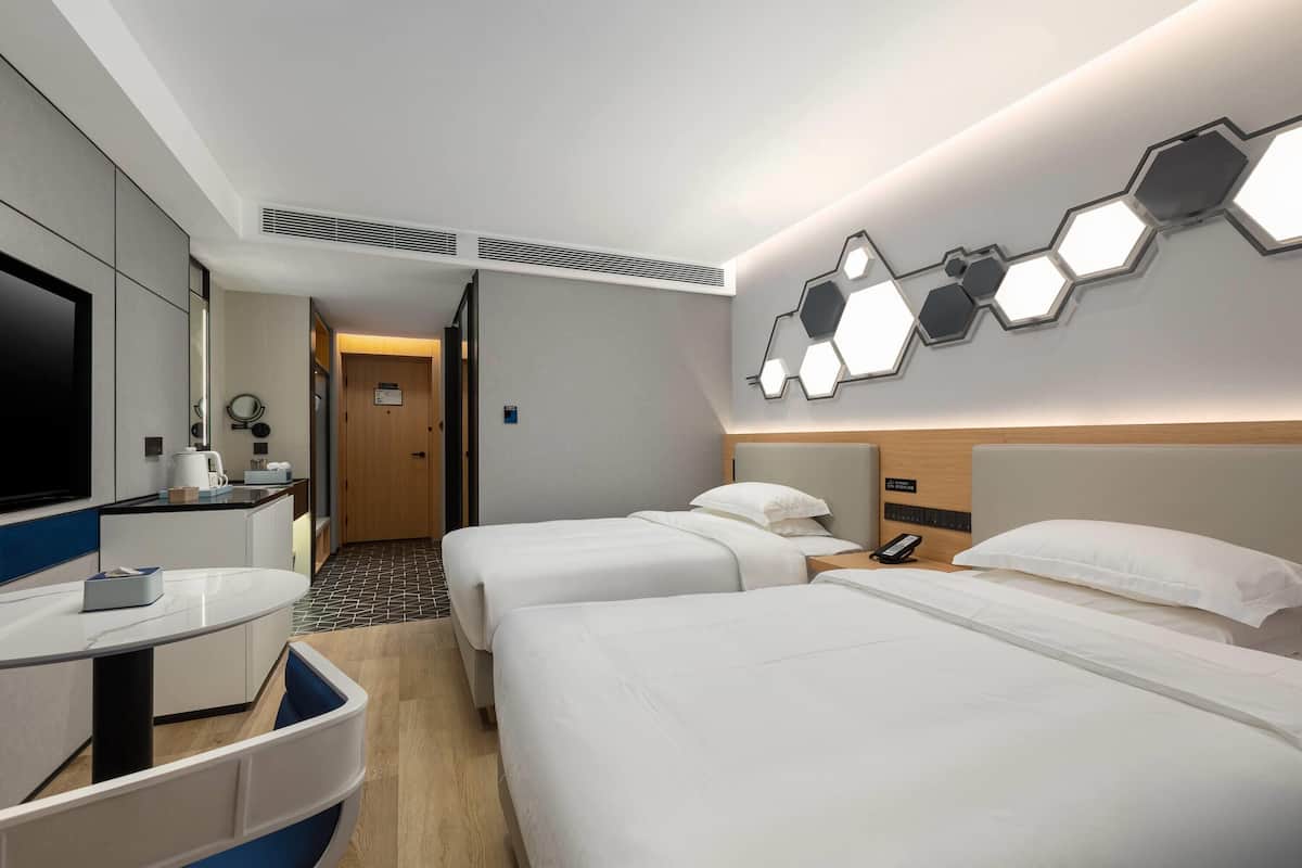 A hotel room with two beds, a desk with a chair, a TV, and a modern wall design.