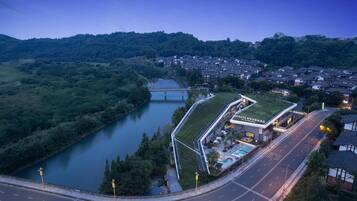 A hotel with a green roof, a swimming pool, and a view of a river and bridge.