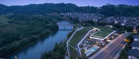 A hotel with a green roof, a swimming pool, and a view of a river and bridge.