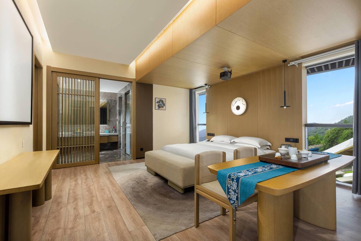 Ein modernes Hotelzimmer mit Bett, Schreibtisch, Stuhl und Blick ins Freie.