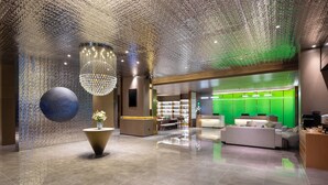 Eine geräumige Lobby mit hoher Decke, einer großen, kugelförmigen Skulptur, einem Chandelier und einem Empfangsbereich mit grüner Beleuchtung.