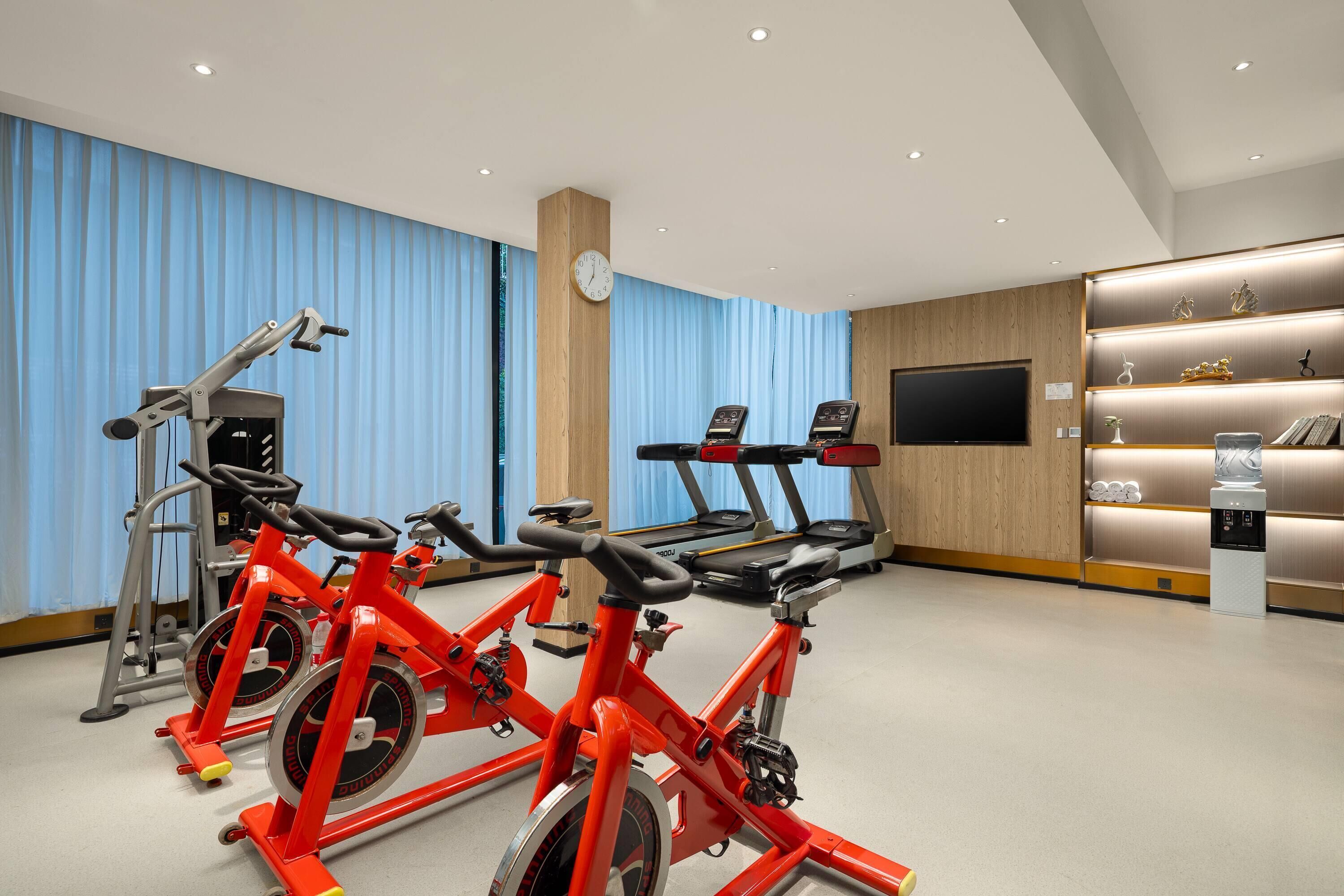 A gym with stationary bikes, treadmills, and a wall-mounted TV.