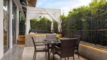 Un patio exterior con mobiliario de mimbre, una mesa y un dosel blanco.