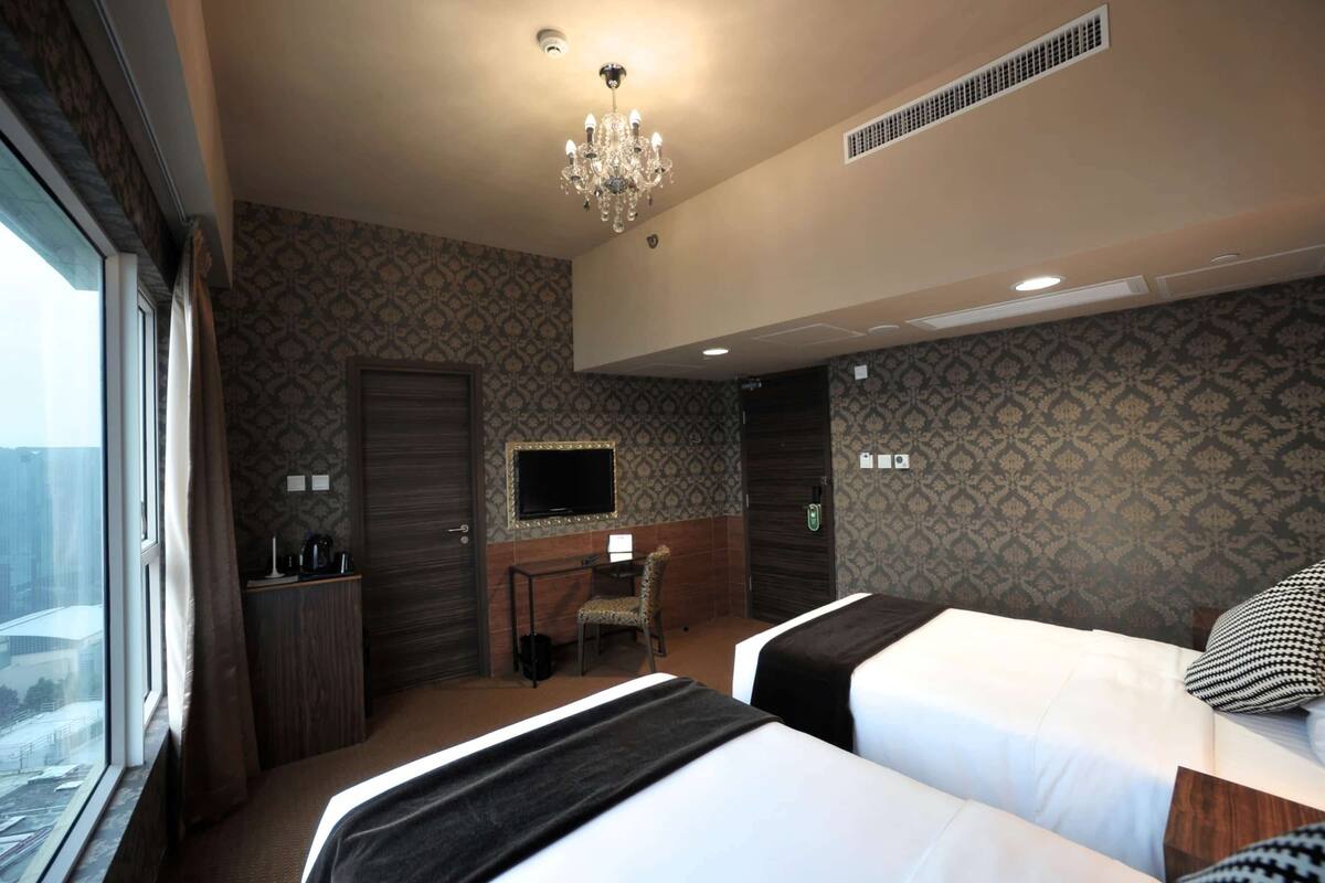 Une chambre d’hôtel avec deux lits, un bureau avec une chaise, une télévision et une fenêtre avec des rideaux.
