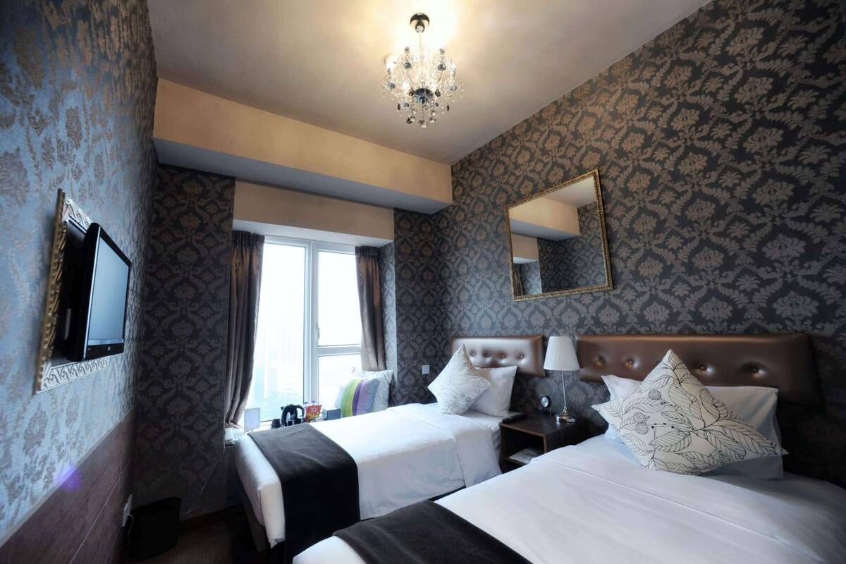 Une chambre d’hôtel avec deux lits, un lustre, un grand miroir et un papier peint à motifs.