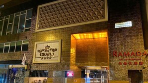 De gevel van een hotel met een opvallend bord waarop 'The Grand' en 'Ramada by Wyndham' staan.