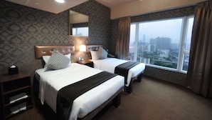 Een hotelkamer met twee bedden, een groot raam met uitzicht op de stad, een kroonluchter en een spiegel aan de muur.