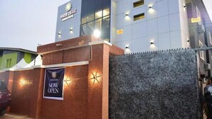 A hotel entrance with a 'NOW OPEN' banner, a gated entrance, and a modern building facade. - White Chase Hotel and Suites (Lagos)