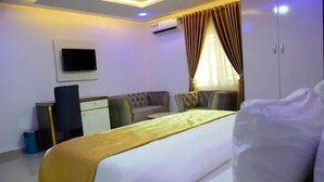 A hotel room with a bed, a desk, a chair, a wardrobe, and a television on the wall. - White Chase Hotel and Suites (Lagos)