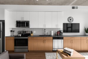 A modern kitchen with white cabinets, stainless steel appliances, and a flat-screen TV mounted on the wall.