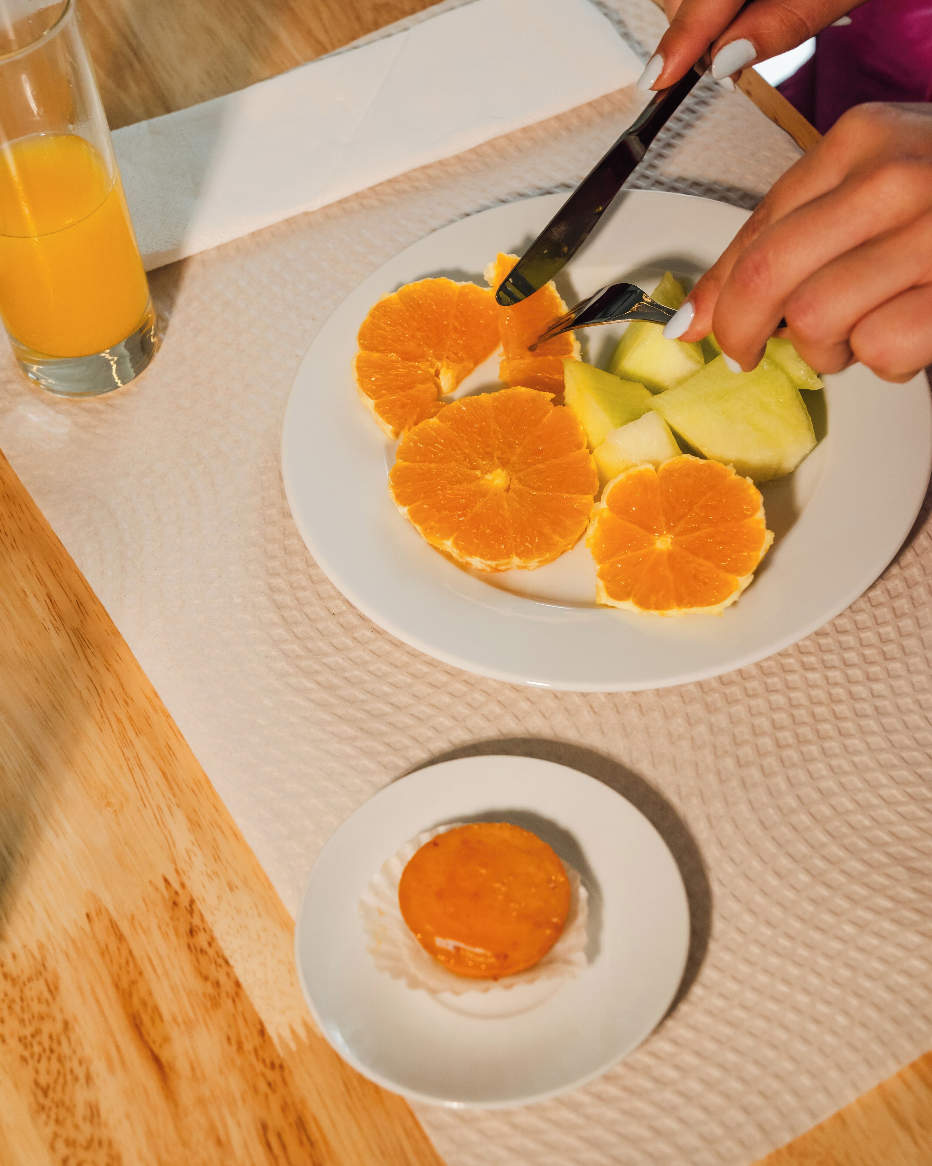 Ein Teller mit Orangenstücken und einem Messer, ein Glas Orangensaft sowie ein kleinerer Teller mit einer einzelnen Orangenscheibe.