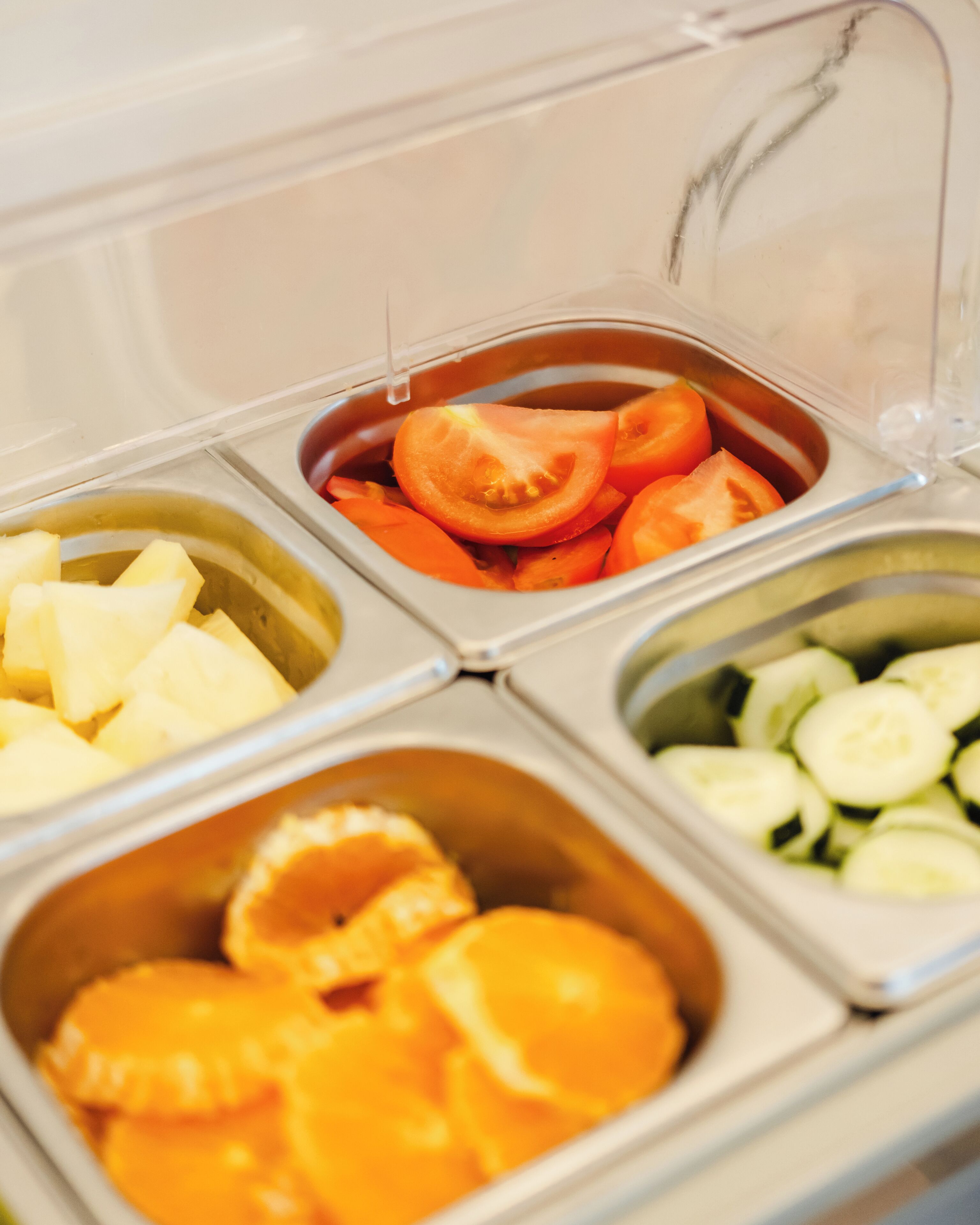 A food storage unit with compartments containing sliced tomatoes, pineapple chunks, orange slices, and cucumber slices.