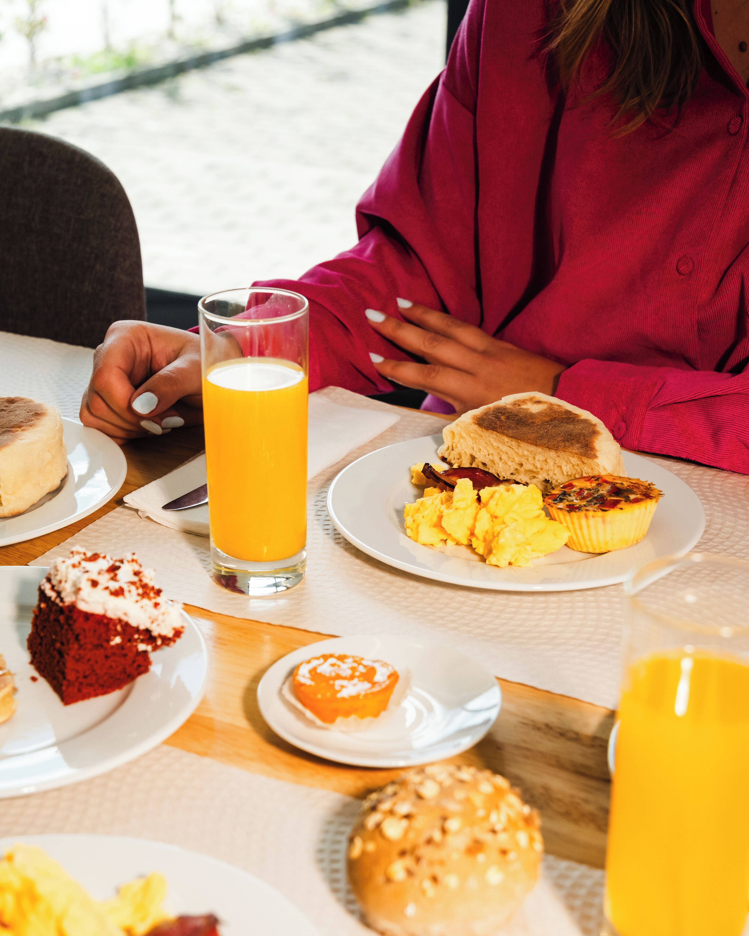 Ein Frühstückstisch mit verschiedenen Speisen, darunter Toast, Rührei und ein Stück Red Velvet Kuchen.