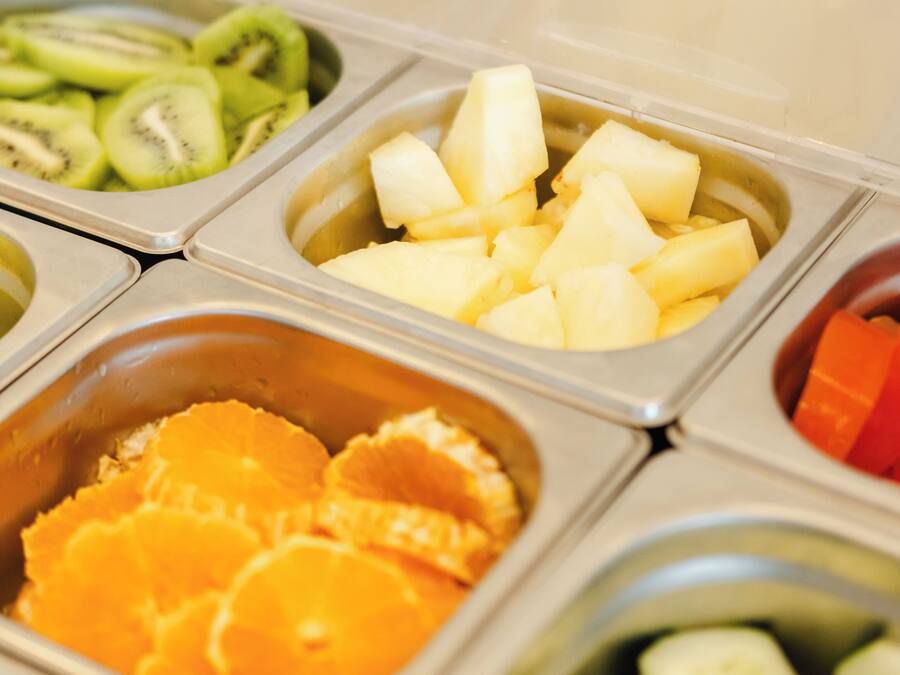 A fruit and vegetable buffet with separate containers for kiwi, pineapple, orange slices, and cucumber.