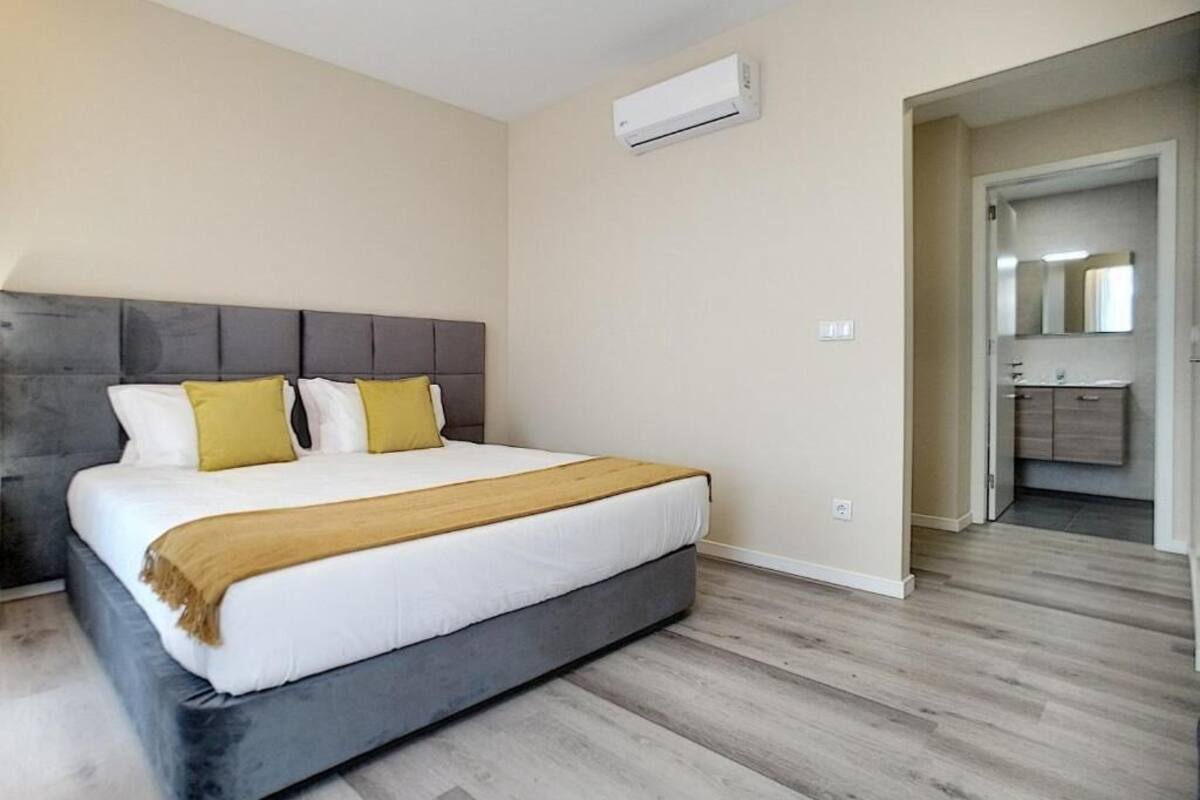 A bedroom with a bed, a headboard, an air conditioning unit, and a wooden floor.