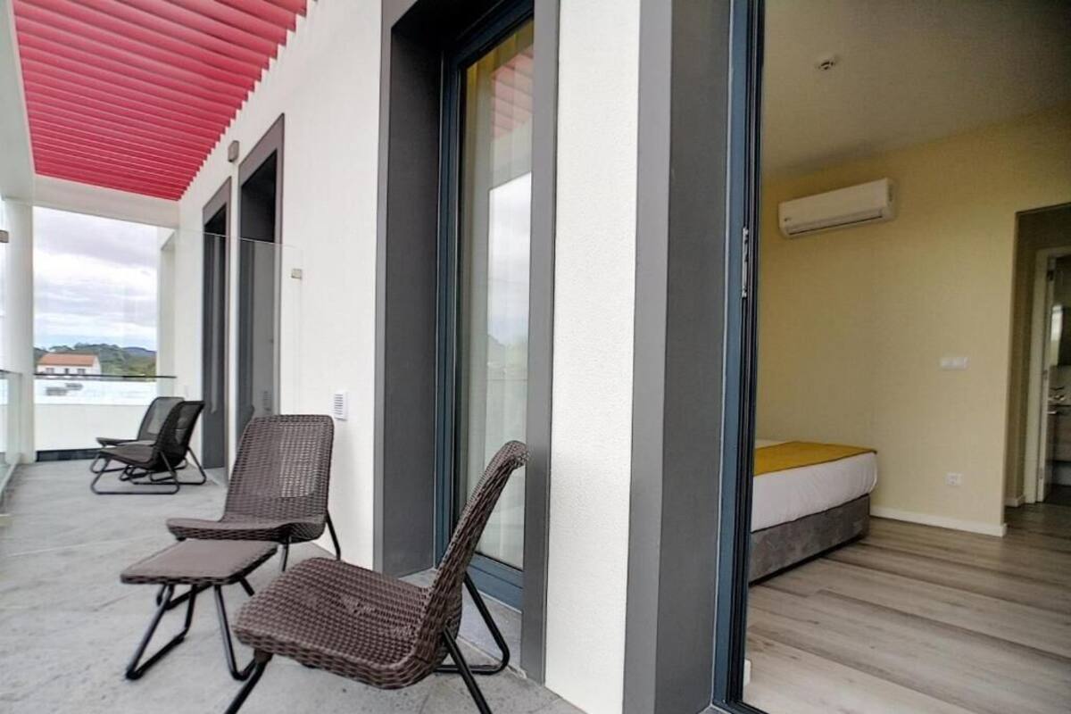 A modern hotel room with a large sliding glass door leading to a balcony with wicker chairs.