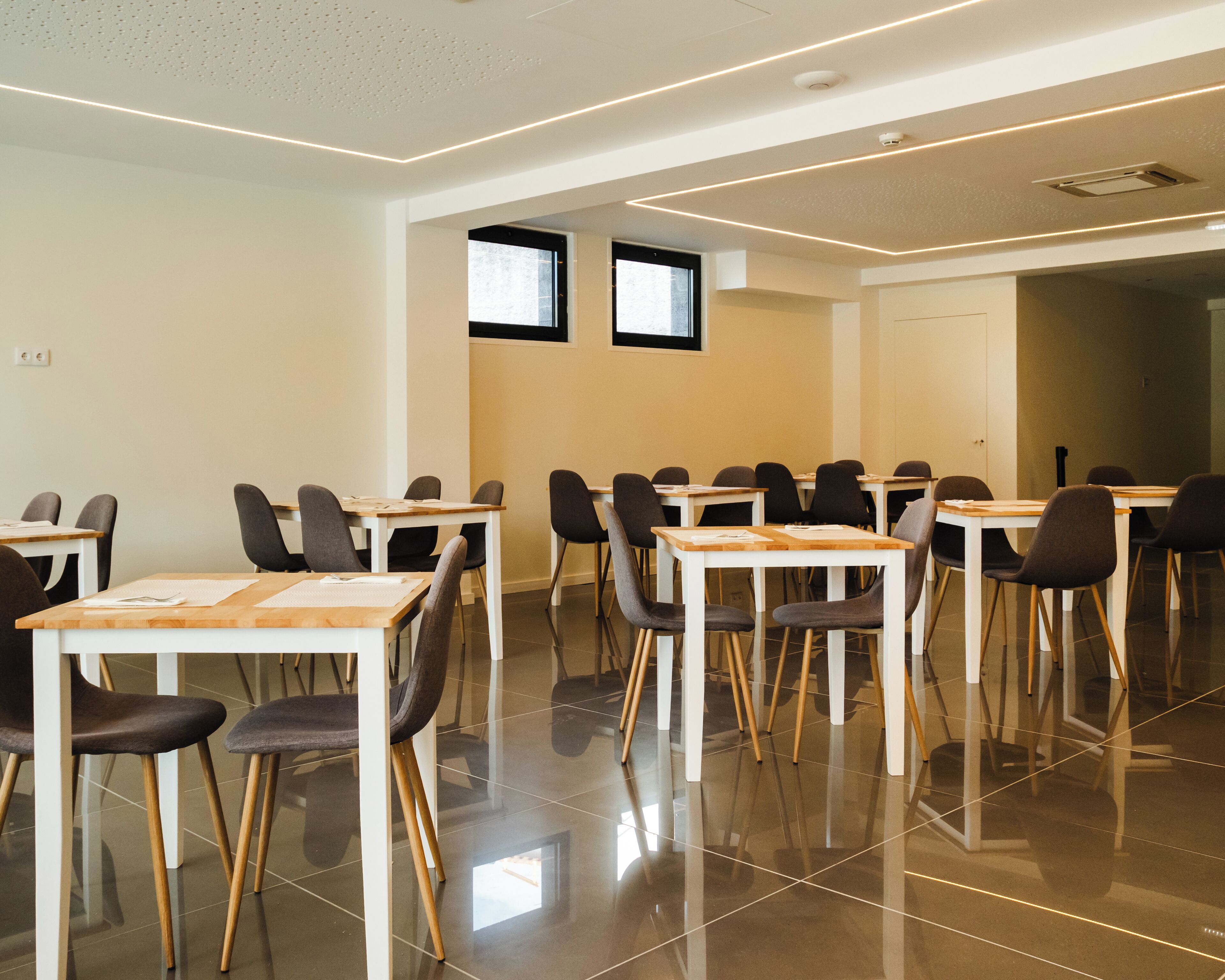 Un salón de conferencias con mesas y sillas, piso de baldosas e iluminación empotrada en el techo.