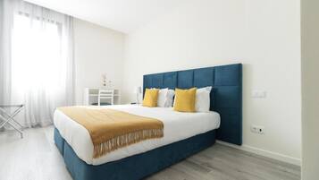 Um quarto moderno com uma cama grande, roupa de cama branca e cabeceira azul.