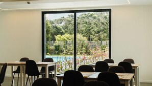 Une salle de conférence équipée de tables et de chaises, de grandes fenêtres donnant sur un jardin et une piscine.
