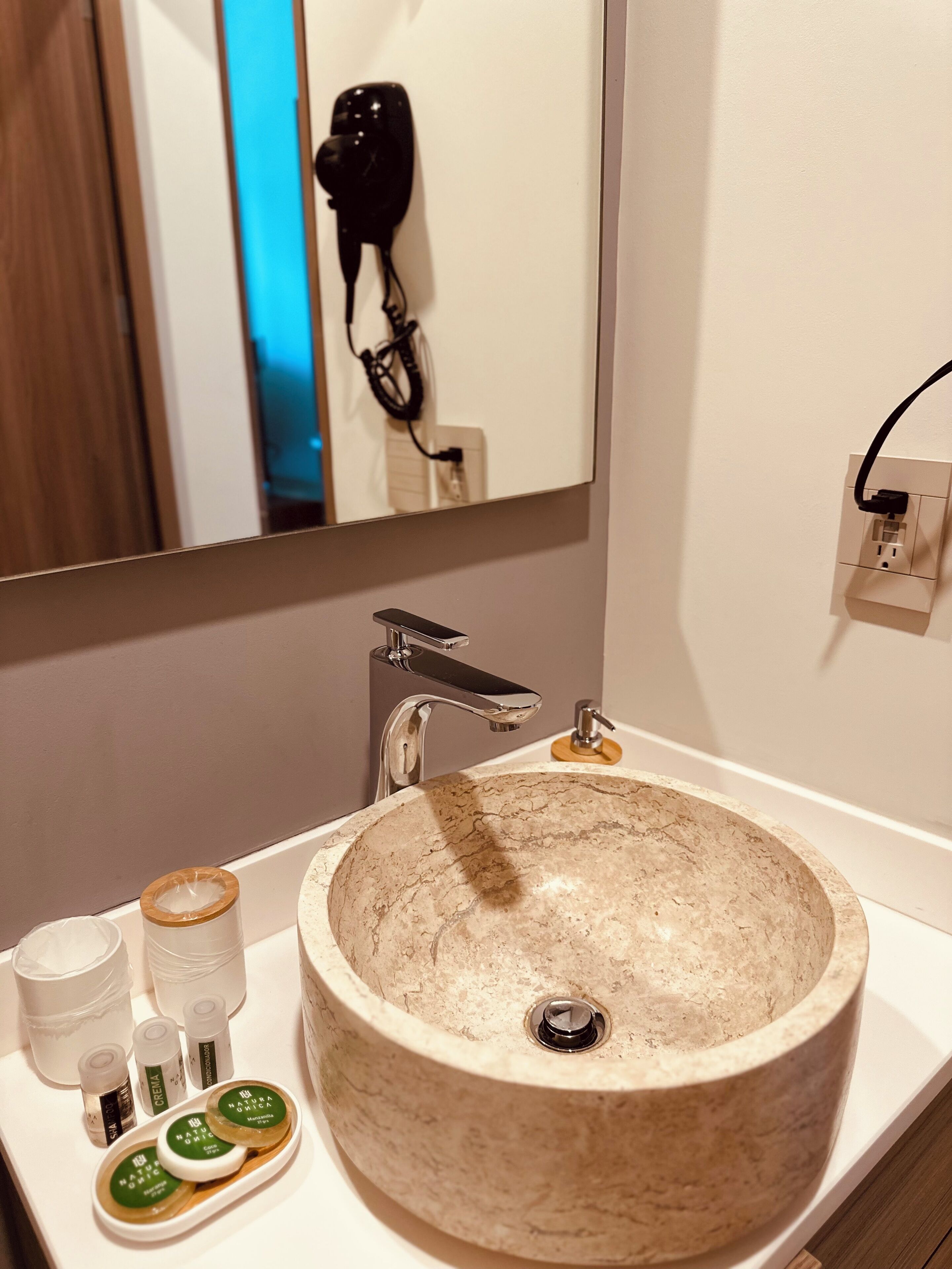 A bathroom with a large beige sink, a mirror, a hairdryer, and toiletries on the counter.