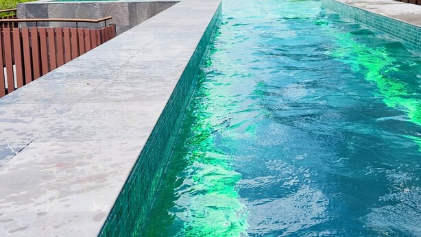 Een zwembad met helderblauw water, omringd door een stenen terras en een houten hek.