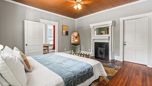 A bedroom with a bed, a ceiling fan, a fireplace, and a door leading to another room.