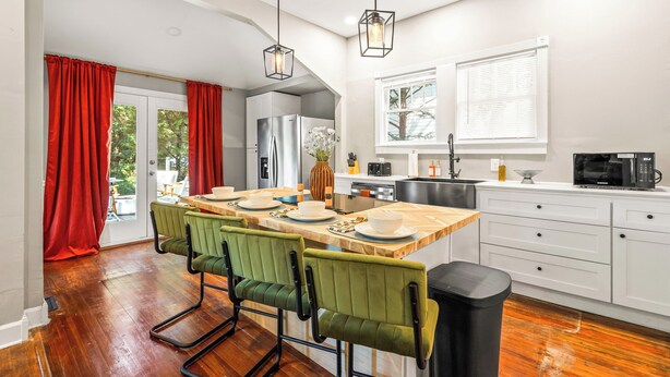 A modern kitchen with a central island, white cabinetry, and a dining area with green chairs.