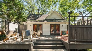 A wooden deck leading to a house with a small porch, outdoor furniture, and a security camera.