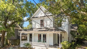 A two-story house with a porch, surrounded by trees and a stone retaining wall.