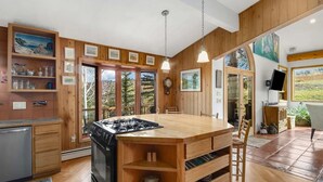 Une cuisine avec des meubles en bois, une cuisinière à gaz et un coin repas avec des chaises.