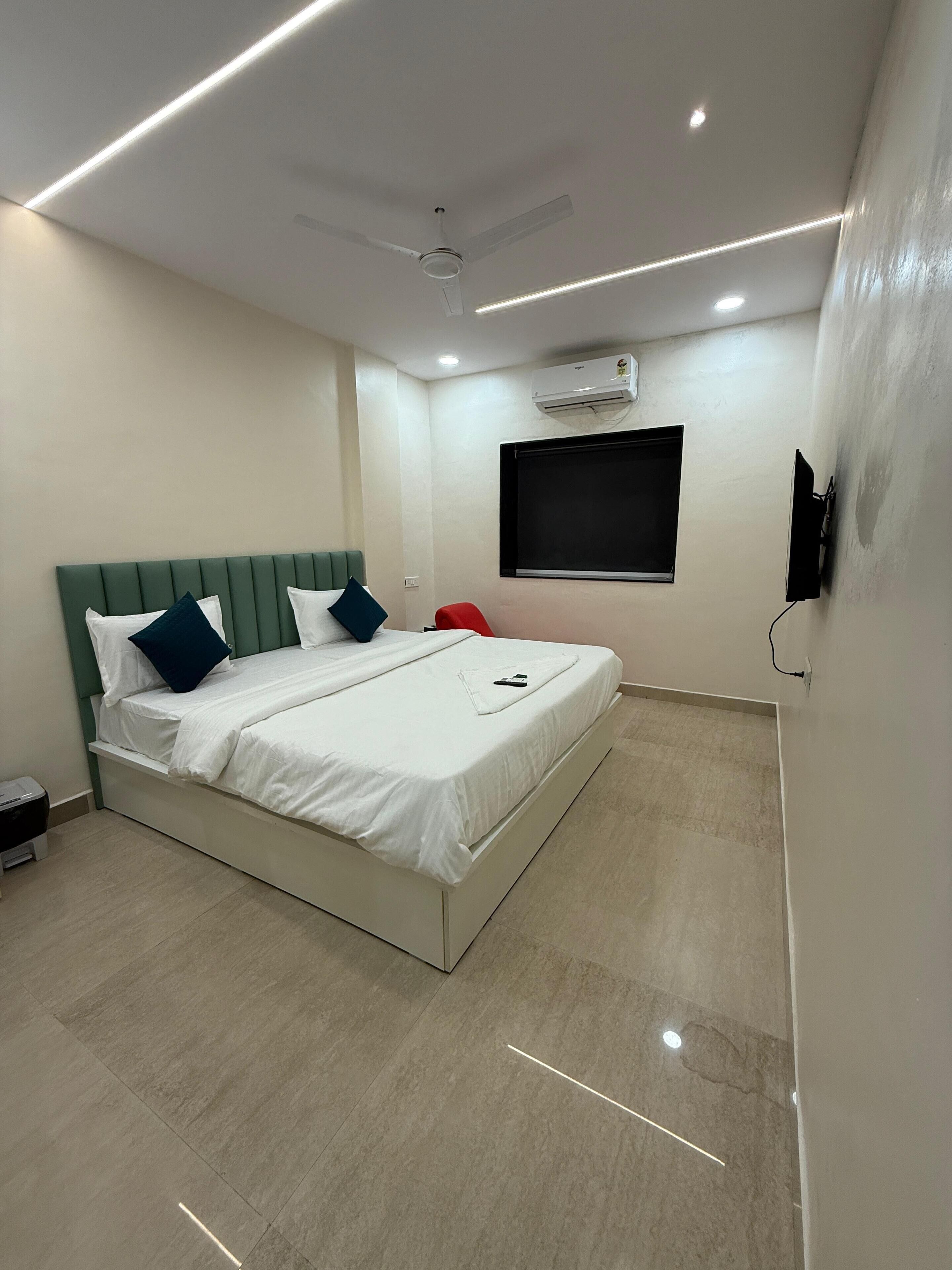 A modern bedroom with a bed, a ceiling fan, recessed lighting, an air conditioning unit, and a mounted TV.