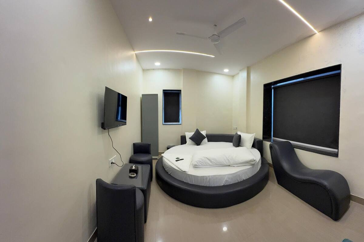 A modern bedroom with a circular bed, a flat-screen TV, a ceiling fan, and a large window.