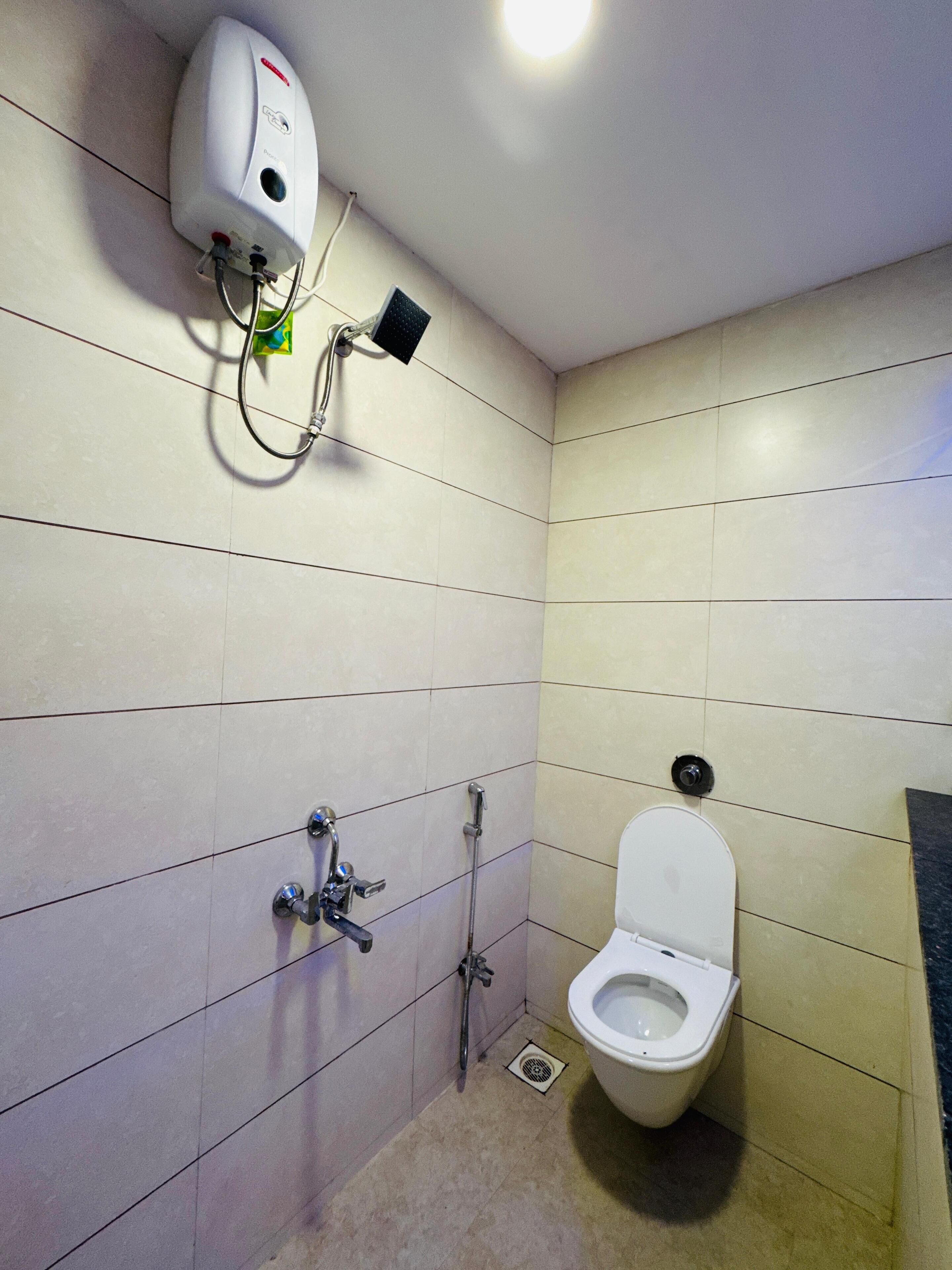 A small, tiled bathroom with a toilet, a hand dryer, and a showerhead.