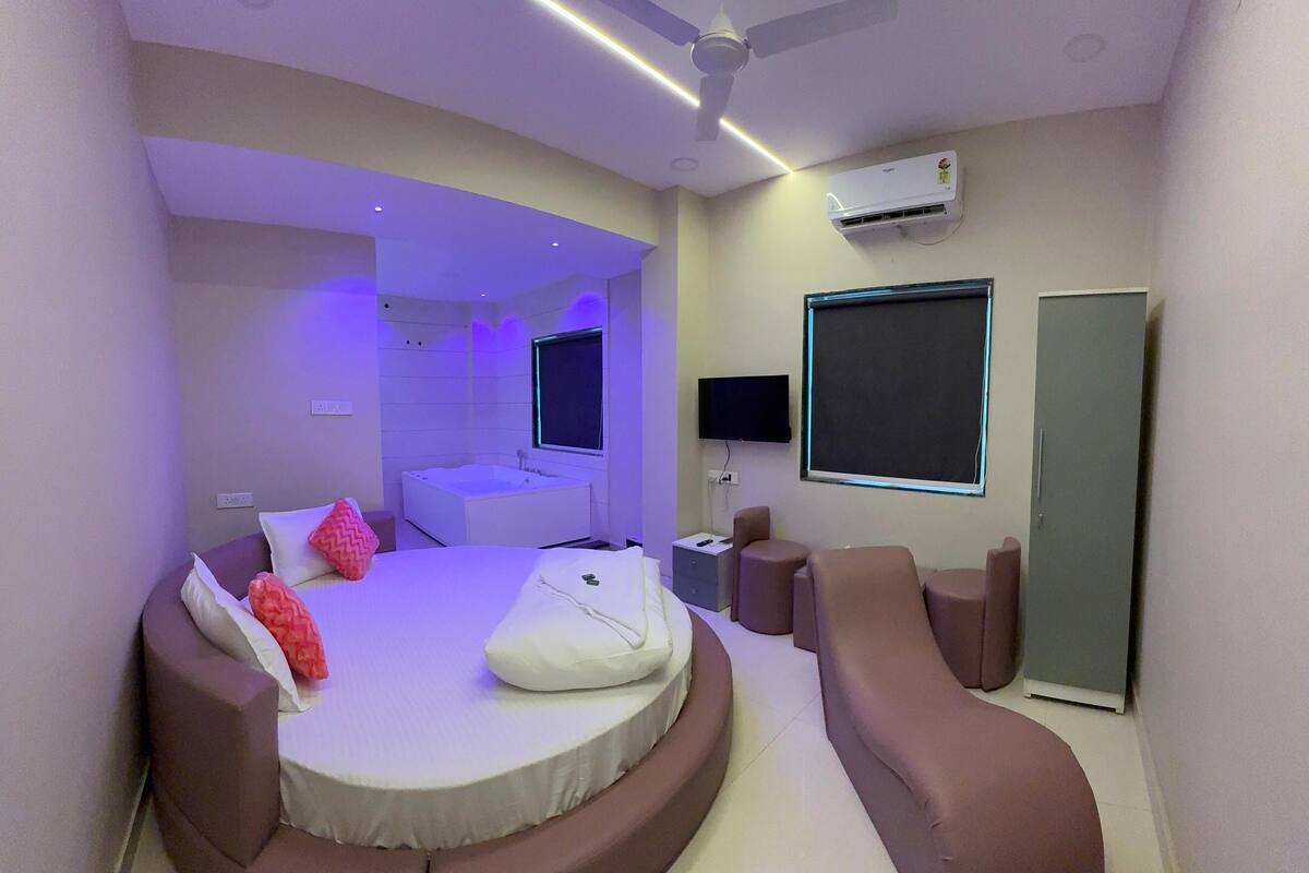A modern bedroom with a curved bed, a TV, a flat-screen TV, a wardrobe, and a ceiling fan.